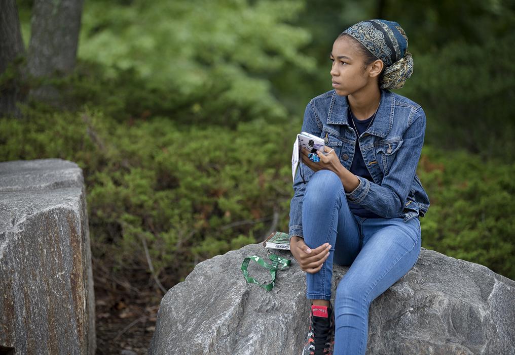 student sitting on a rock holding her mobile phone